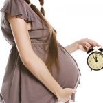 Беременная женщина держит часы