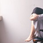 Женщина сидит на стуле напротив окна и плачет