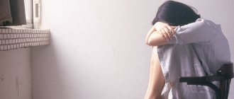 A woman sits on a chair opposite the window and cries